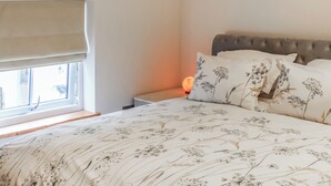 Een slaapkamer met een bed, een raam met een jaloezie, een nachtkastje met een lamp en een hoofdbord.