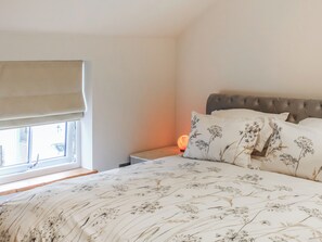 A bedroom with a bed, a window with a blind, a bedside table with a lamp, and a headboard. - The Pump House - UK50648 (Falmouth)