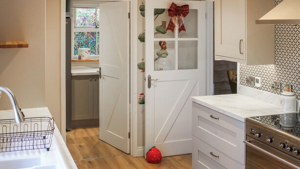 Een keuken met witte kastjes, een roestvrijstalen spoelbak, een houten vloer en een decoratieve deur met een strik.