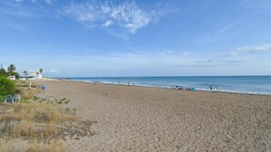 Ein Strand mit klarem Himmel, sandigem Ufer und ein paar Personen in der Ferne.