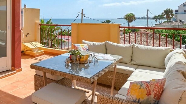 Ein Balkon mit einem Korbstuhl, einem weißen Sofa und Blick aufs Meer.