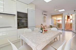 A modern kitchen with white cabinetry, a dining area with a table set for two, and a view of a balcony. - Denimar 4 pax - Denia, Costa Blanca (Denia)