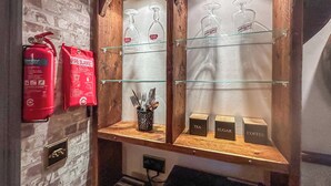 A bar area with shelves displaying glasses, a fire extinguisher, and labeled containers for tea, sugar, and coffee. - Marton Lodge Apartment (Bridlington)