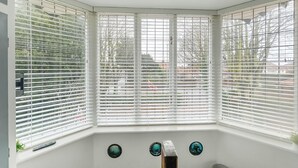 A bay window with white blinds, a remote control, and decorative plates on the sill. - Marton Lodge Apartment (Bridlington)