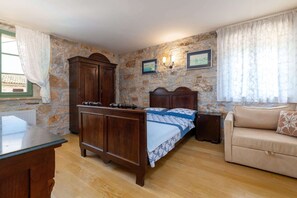 A bedroom with a wooden bed, a stone wall, a wooden cabinet, a sofa, and a window with curtains. - Villa Rosini (100051-K1) - Porec (Porec)