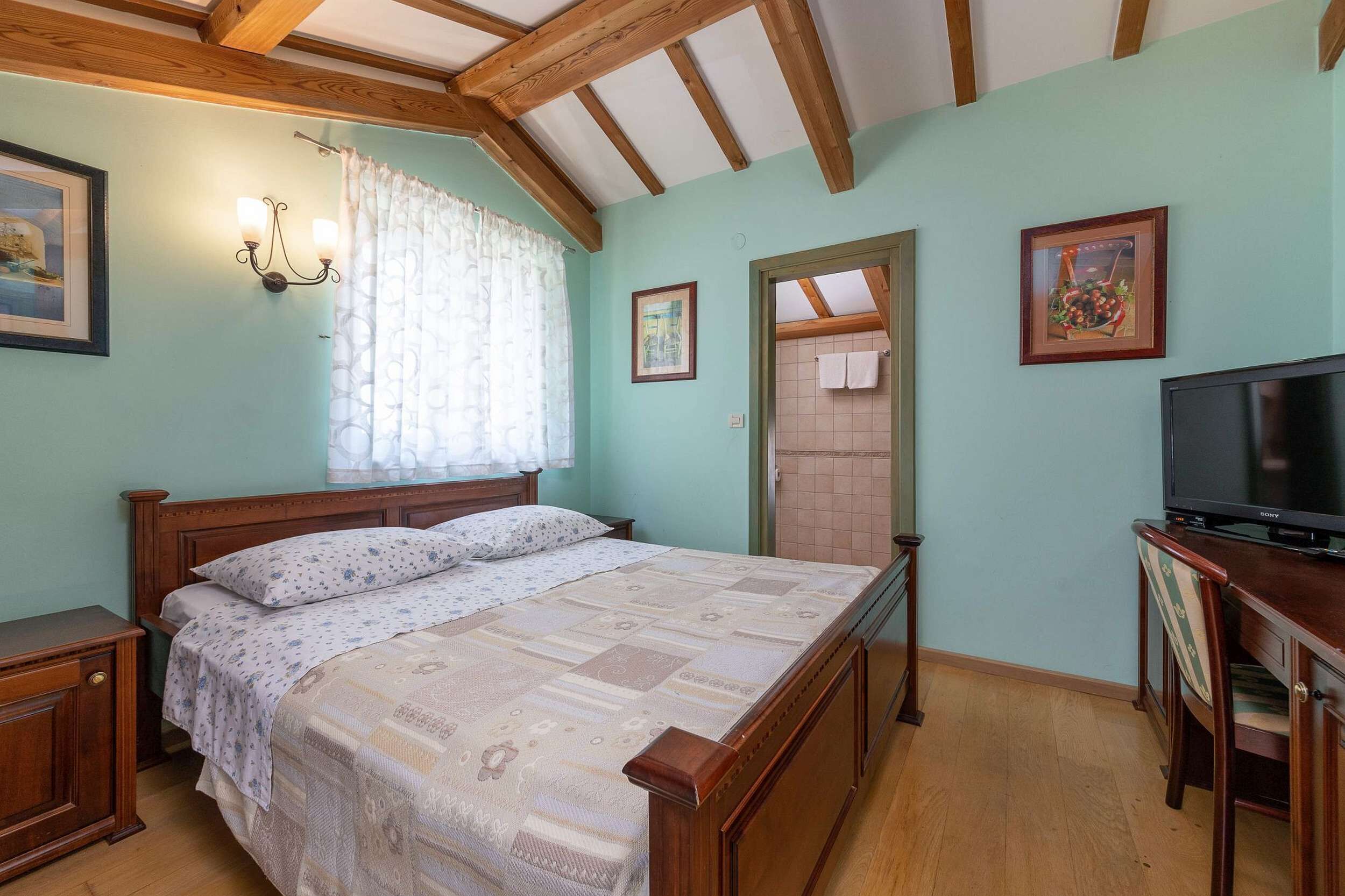 Ein Schlafzimmer mit einem hölzernen Bett, einem Fernseher und einem Fenster mit Vorhängen.