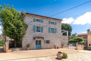 A stone building with a blue door and shutters, a paved courtyard, and a large tree. - Villa Rosini (100051-K1) - Porec (Porec)