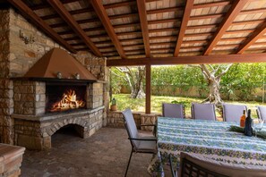 An outdoor patio with a stone fireplace, wooden ceiling beams, and a table set for dining. - Villa Rosini (100051-K1) - Porec (Porec)