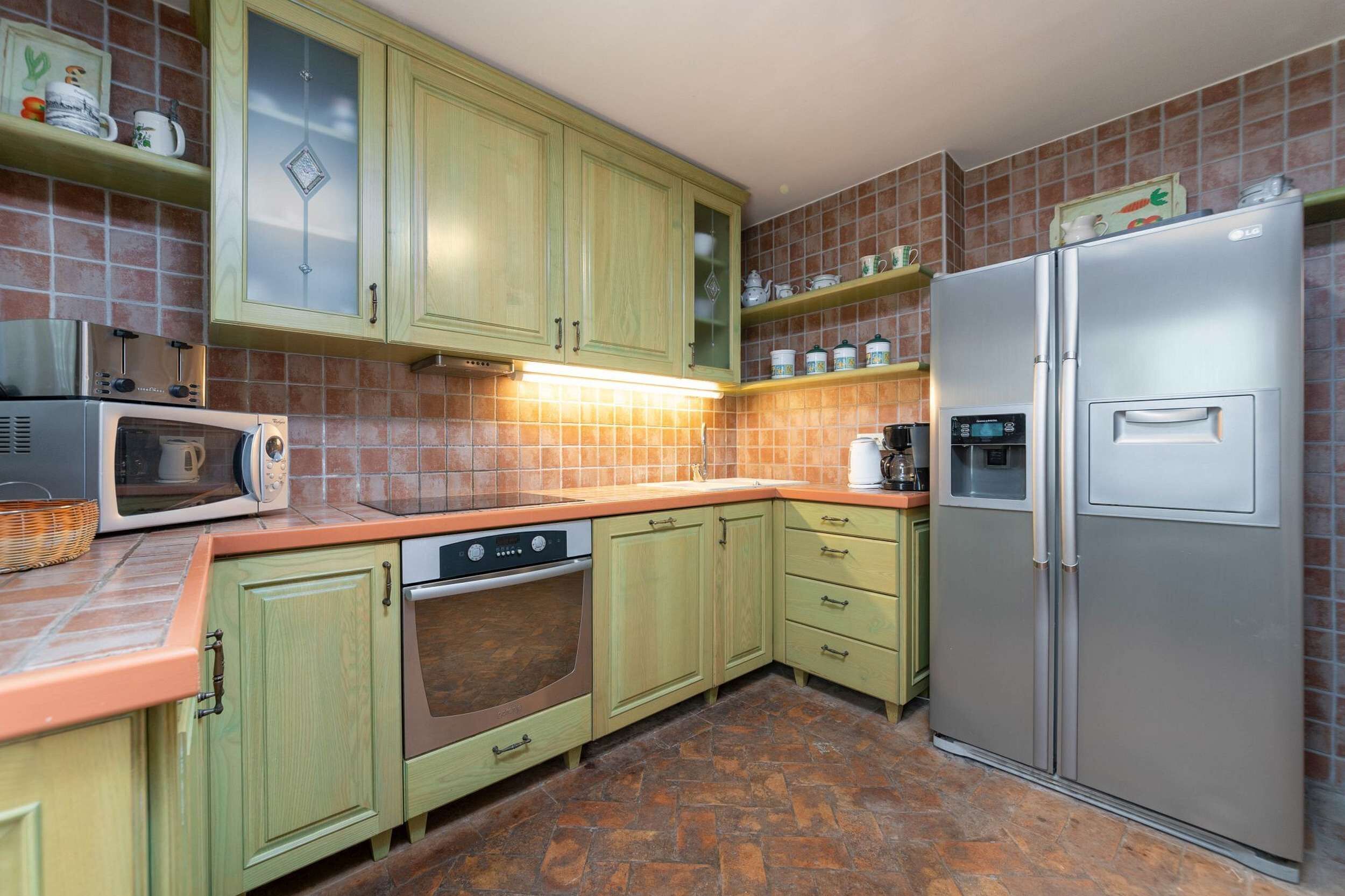 Une cuisine avec des meubles de couleur verte, un four à micro-ondes, un four traditionnel, un réfrigérateur et un dosseret carrelé.
