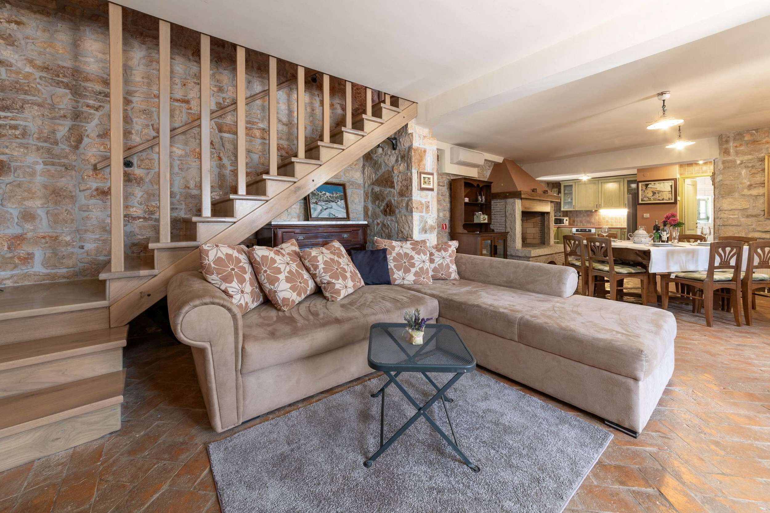 Un salon avec un canapé d’angle beige, une petite table basse noire et un escalier en pierre.