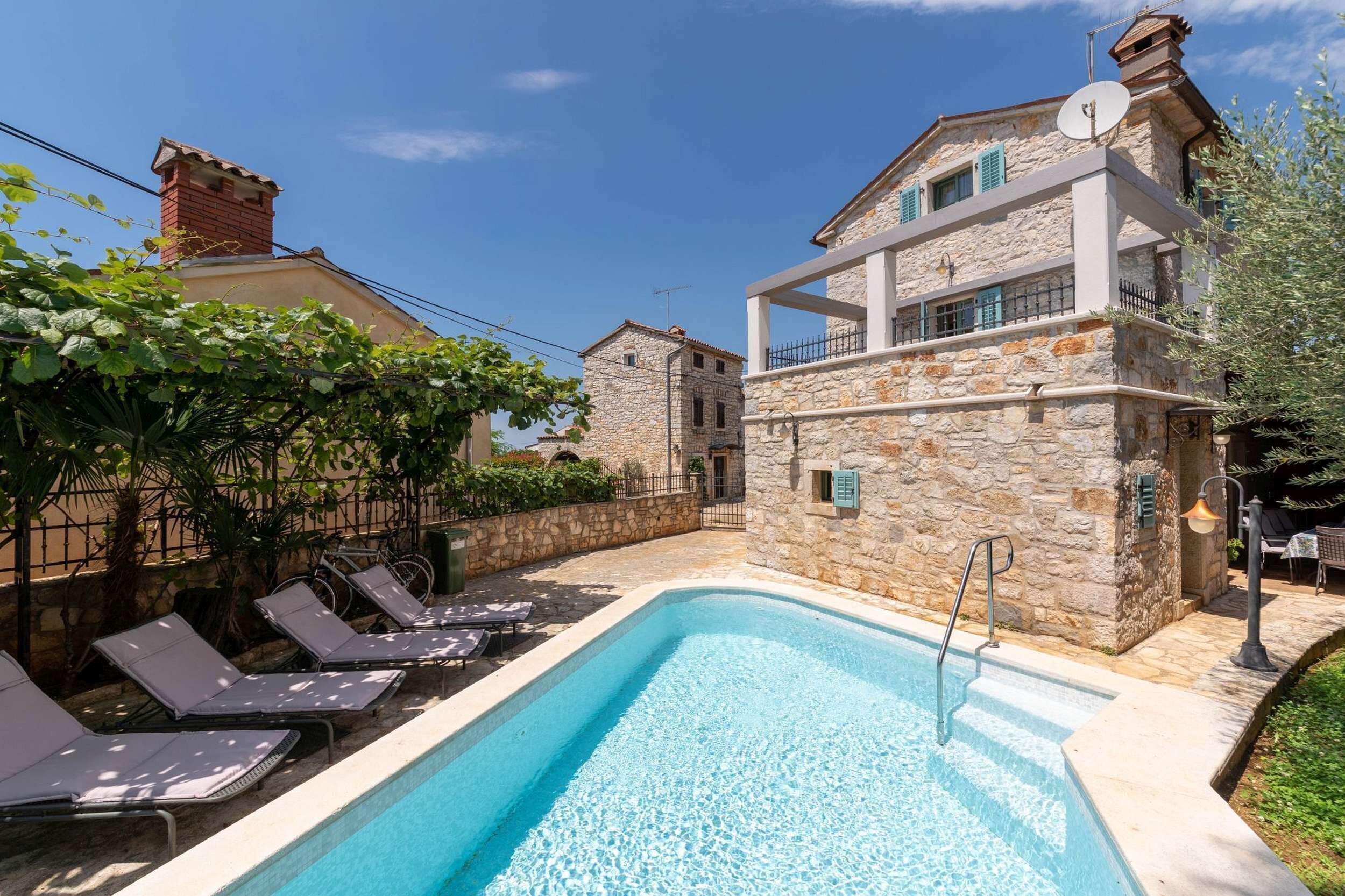 A swimming pool with lounge chairs, stone buildings, and a clear sky.