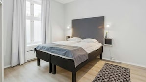 A modern bedroom with a bed, curtains, a bedside table with a lamp, and a patterned rug. - Oslo Apartments Observatoriegaten (Oslo)