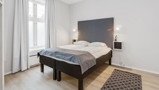 A modern bedroom with a bed, curtains, a bedside table, a wall-mounted light, and a patterned rug. - Oslo Apartments Observatoriegaten (Oslo)