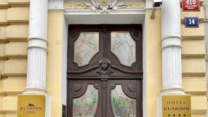 Une double porte en bois, ornée de panneaux de verre, flanquée de deux plantes en pot, et portant des panneaux indiquant «Hôtel Klarinn» et «Résidence».