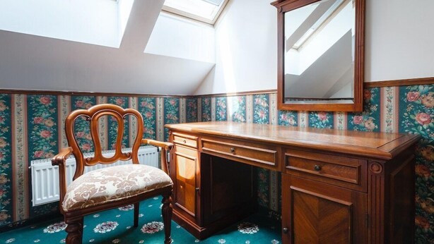 Une pièce avec un bureau en bois, une chaise, un grand miroir et un papier peint à motifs floraux.