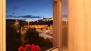 Une vue depuis une fenêtre, avec un vase de roses rouges, donnant sur un paysage urbain où les bâtiments sont illuminés et une route où l’on aperçoit des traînées de lumière.
