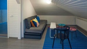 A compact room with a gray sofa, colorful cushions, a small table, and a chair. - Hotel Gardur (Reykjavik)