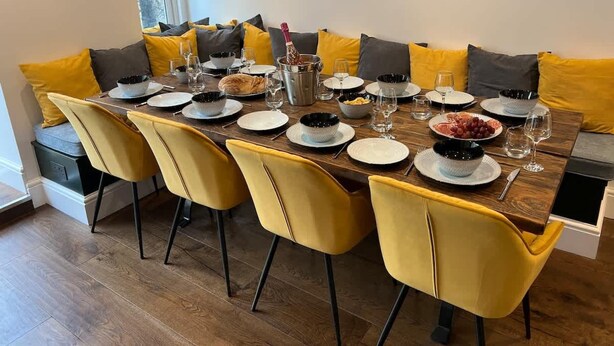 A dining table set for six with yellow chairs, a wooden table, and various dishes and glasses. - Stunning Luxury Holiday Home in Bath (Bath)