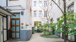 Un patio con un sendero de ladrillo, una puerta de madera y un pequeño jardín con árboles y arbustos.