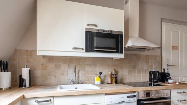 Una cocina moderna con armarios blancos, lavavajillas de acero inoxidable, horno Bosch y microondas negro.