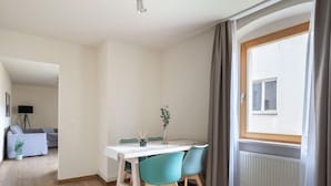 Un comedor con una mesa blanca y sillas color turquesa, una planta en maceta y una ventana con cortinas.