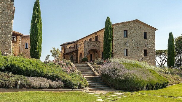 Un bâtiment en pierre avec un escalier menant à une porte, entouré de jardins bien entretenus et de grands arbres.
