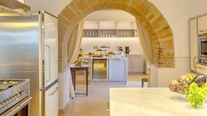 Une cuisine moderne avec un élément décoratif en briques en forme d’arc, des appareils en acier inoxydable et un îlot central doté d’un évier et d’un plan de travail.