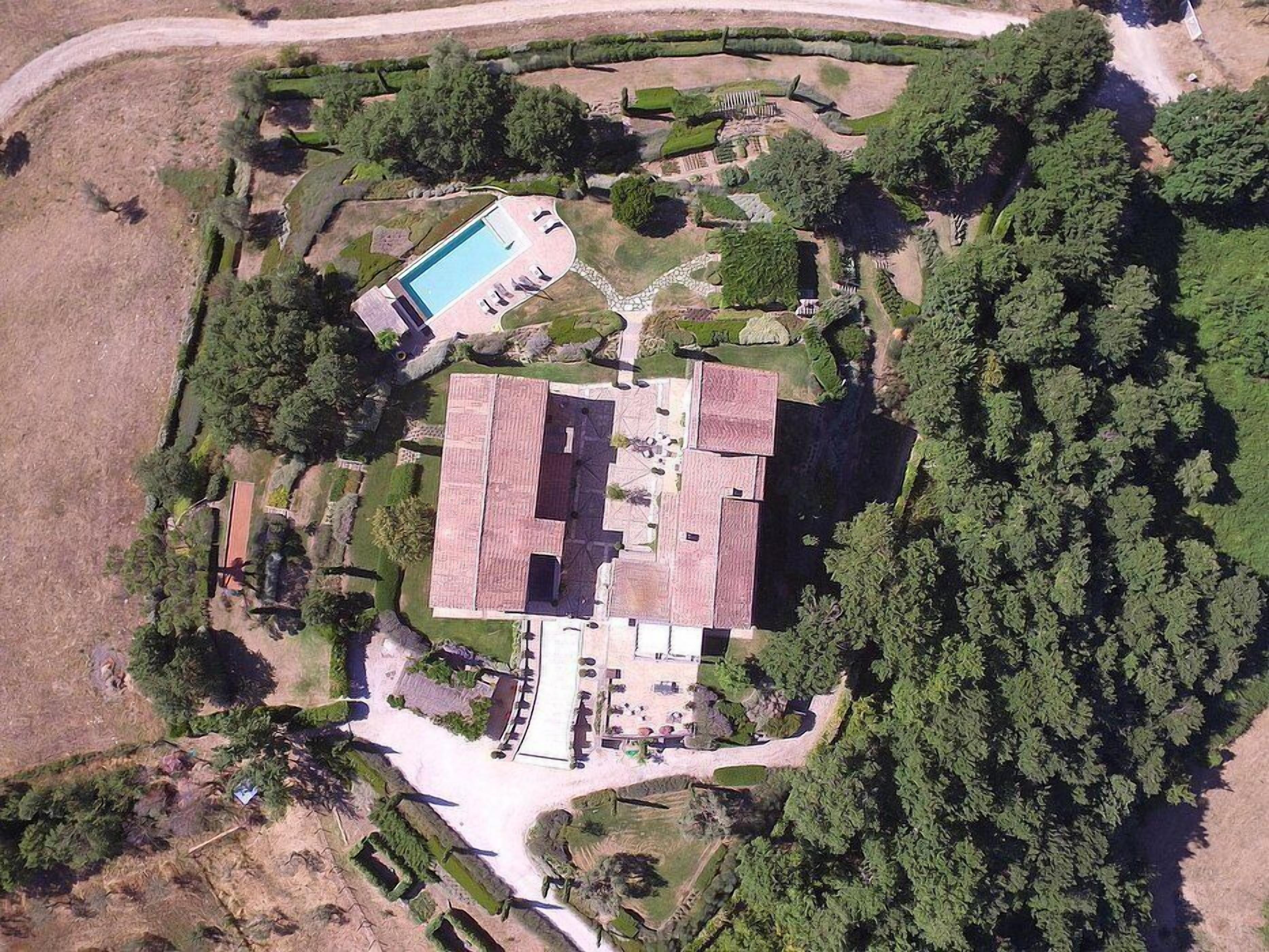 An aerial view of a large estate with a swimming pool, multiple buildings, and extensive landscaping.