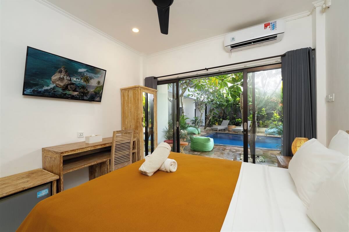 Une chambre d’hôtel avec un lit, un bureau, une chaise, un tableau et une vue sur une piscine extérieure.