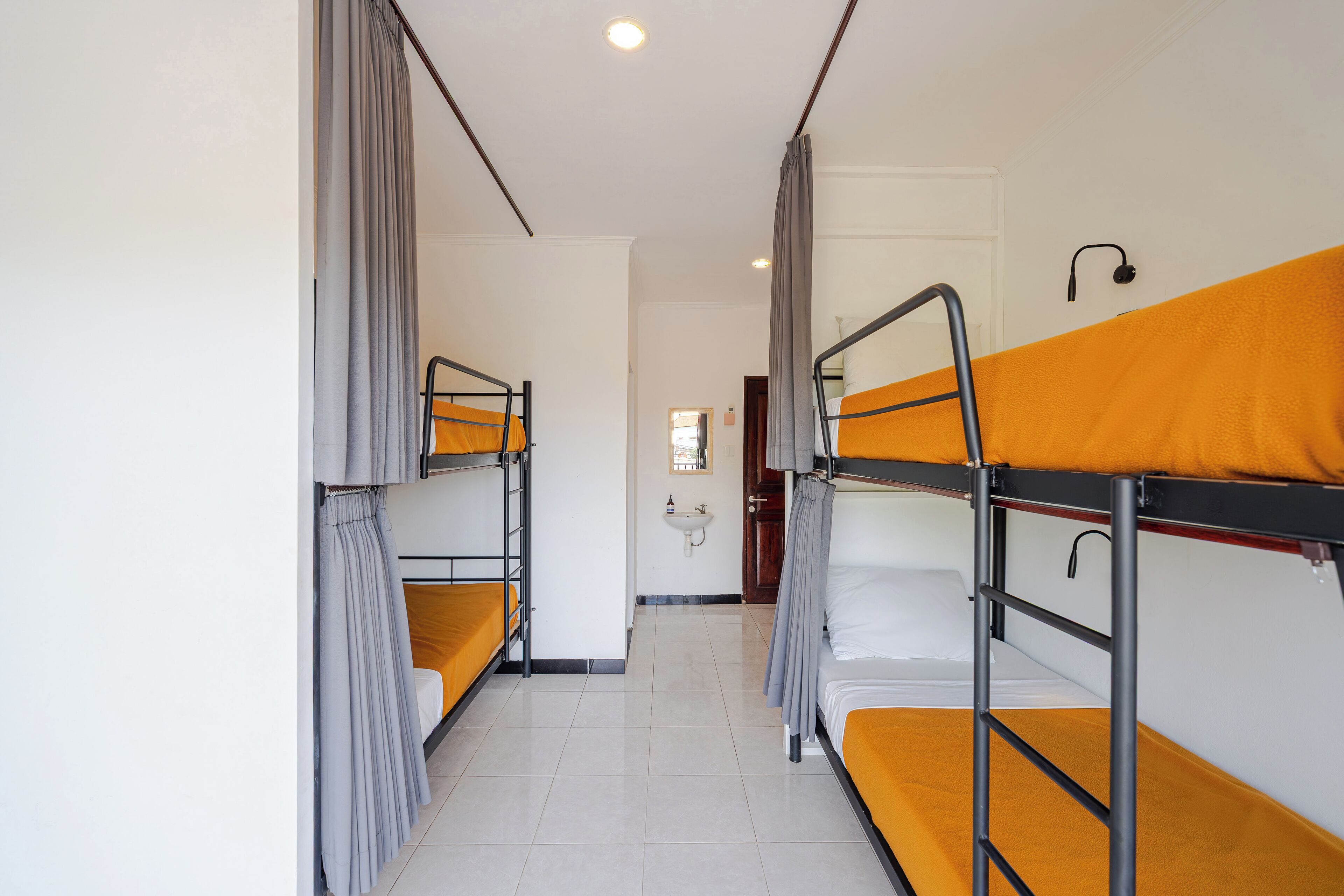 Un couloir avec des lits superposés, un lavabo et une porte au fond.