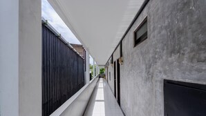 A narrow corridor with a tiled floor, white walls, and a dark fence on one side. - Uluwatu Surf Paradise (Ungasan)