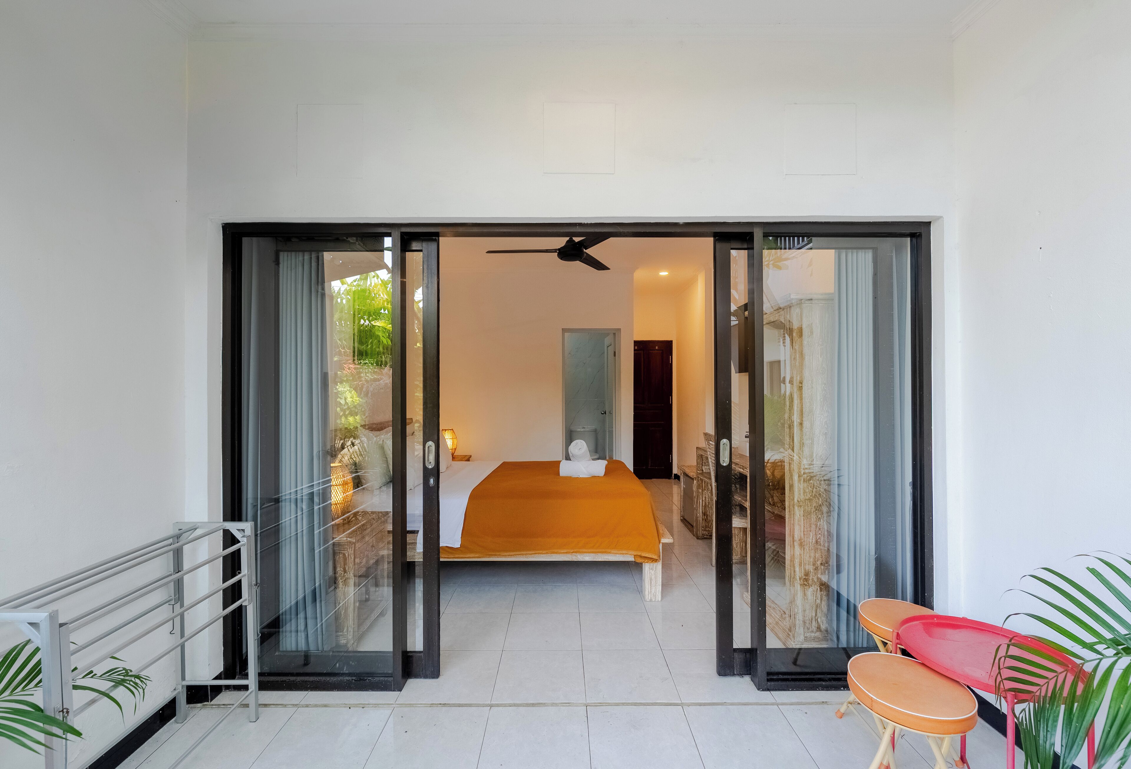 A modern bedroom with a bed, a ceiling fan, and a view through a glass door.