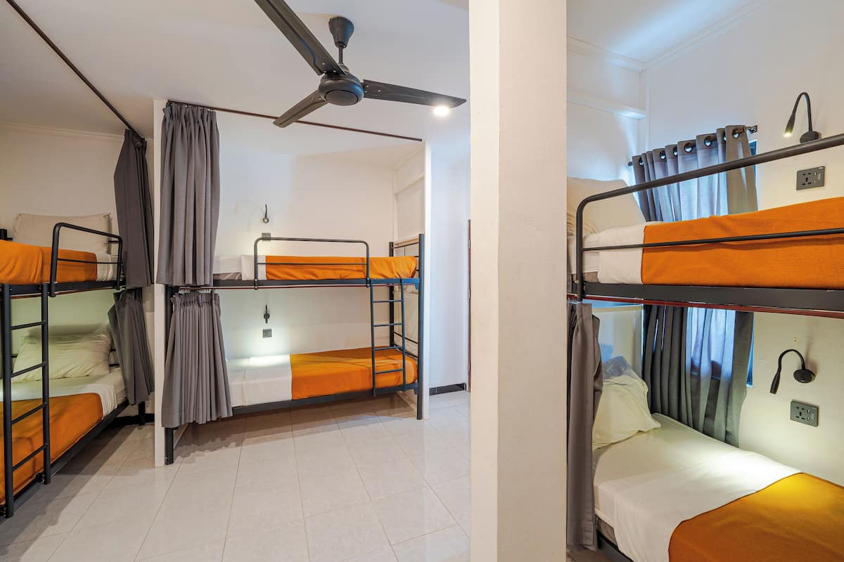 Une chambre de dortoir avec des lits superposés, un ventilateur de plafond et une prise électrique au mur.