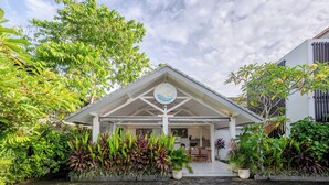 A modern building with a covered entrance, surrounded by lush greenery and a clear sky. - Uluwatu Surf Paradise (Ungasan)