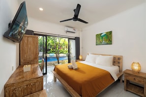 Habitación de hotel con cama, televisión, ventilador de techo, un cuadro y vista a una piscina.
