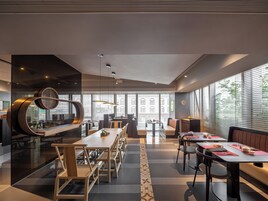 A modern restaurant with a long communal table, individual booths, and a bar area.