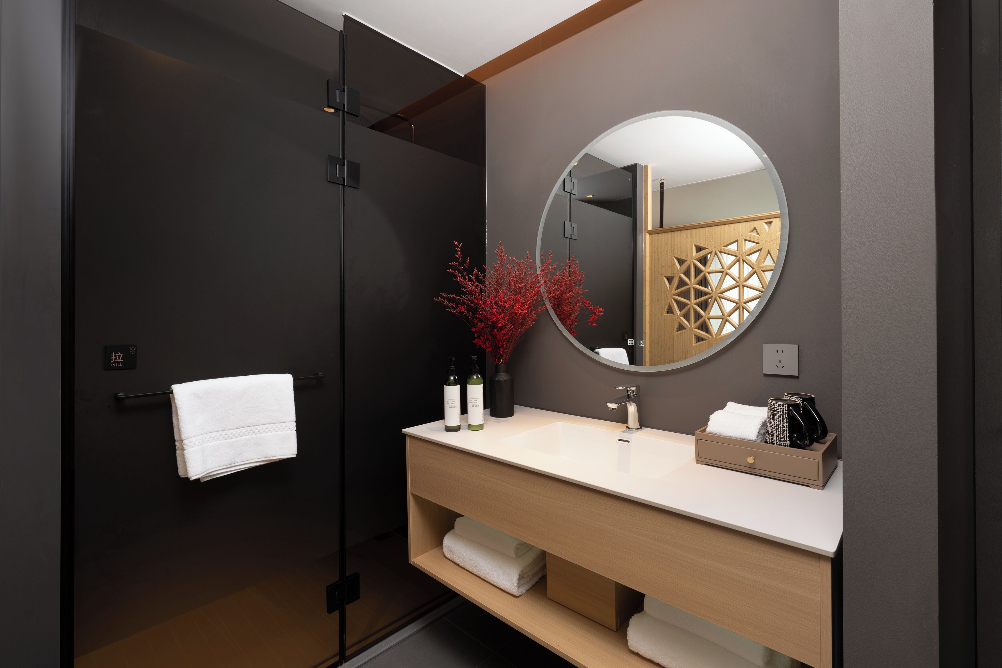 Une salle de bain moderne avec une porte sombre, un lavabo blanc, un miroir et un porte-serviettes.