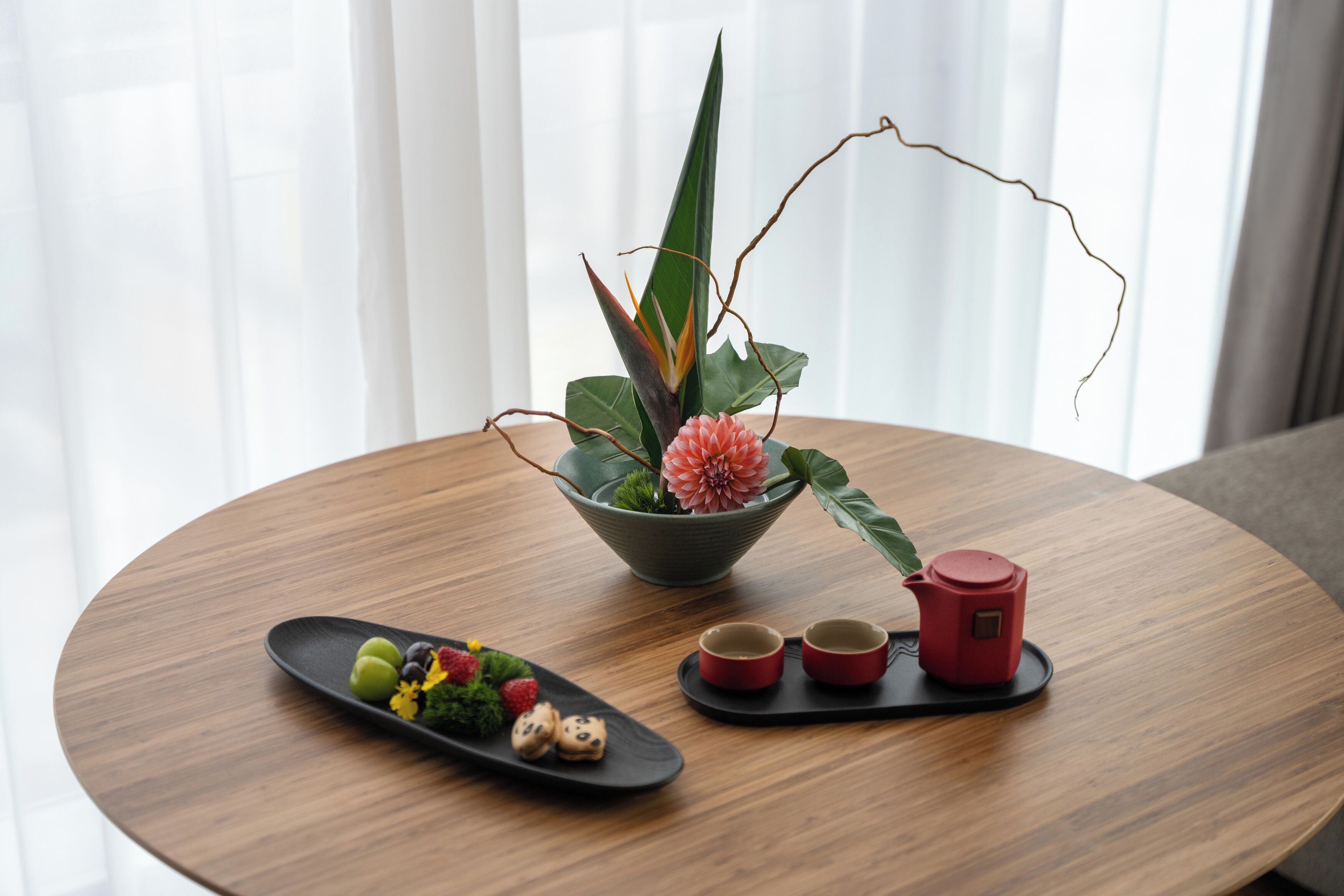 A round wooden table with a decorative plant, a small dish of food, and two red cups.