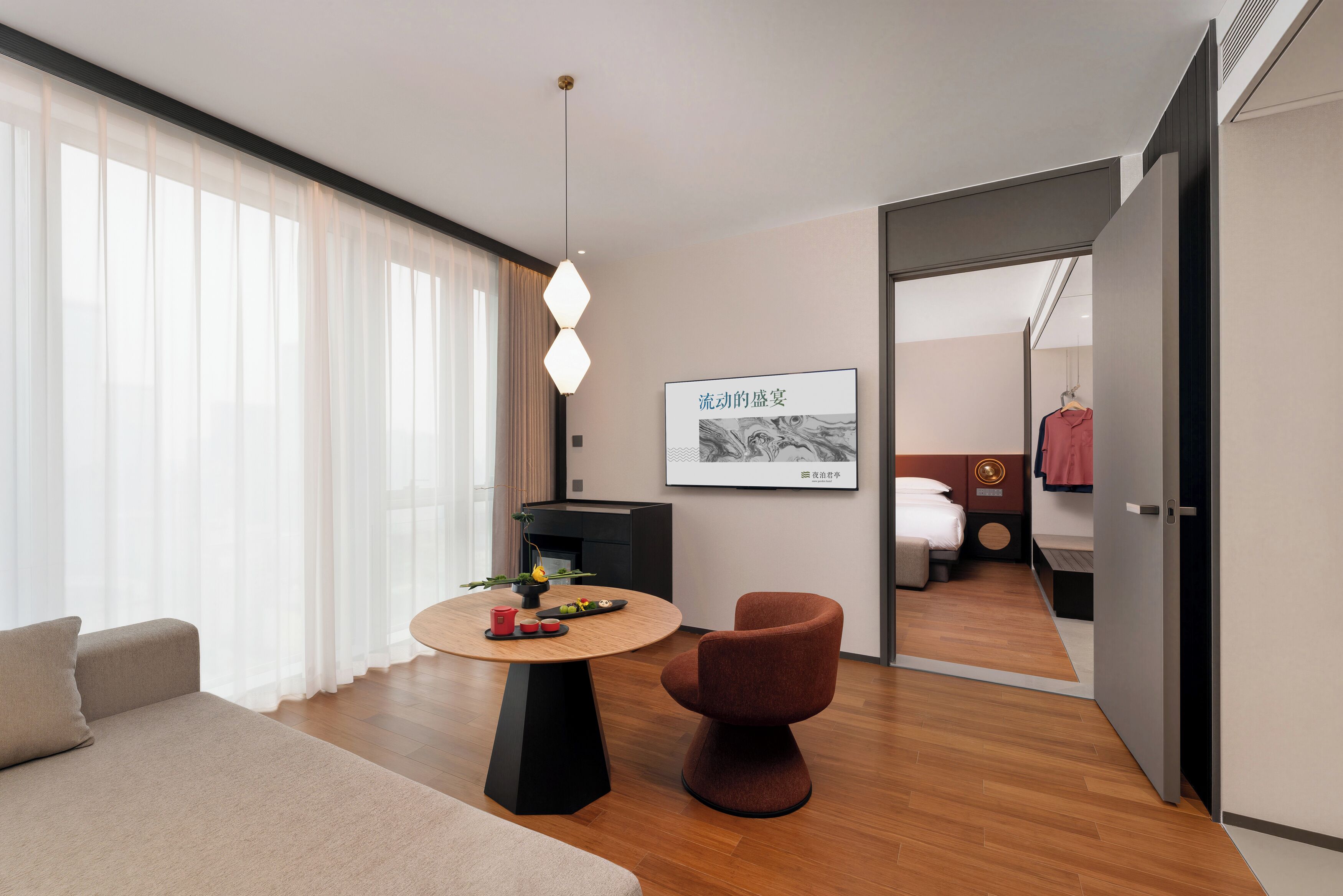 Una habitación de hotel moderna con una mesa redonda de madera, un sofá cómodo, una silla roja, una cama y un armario.