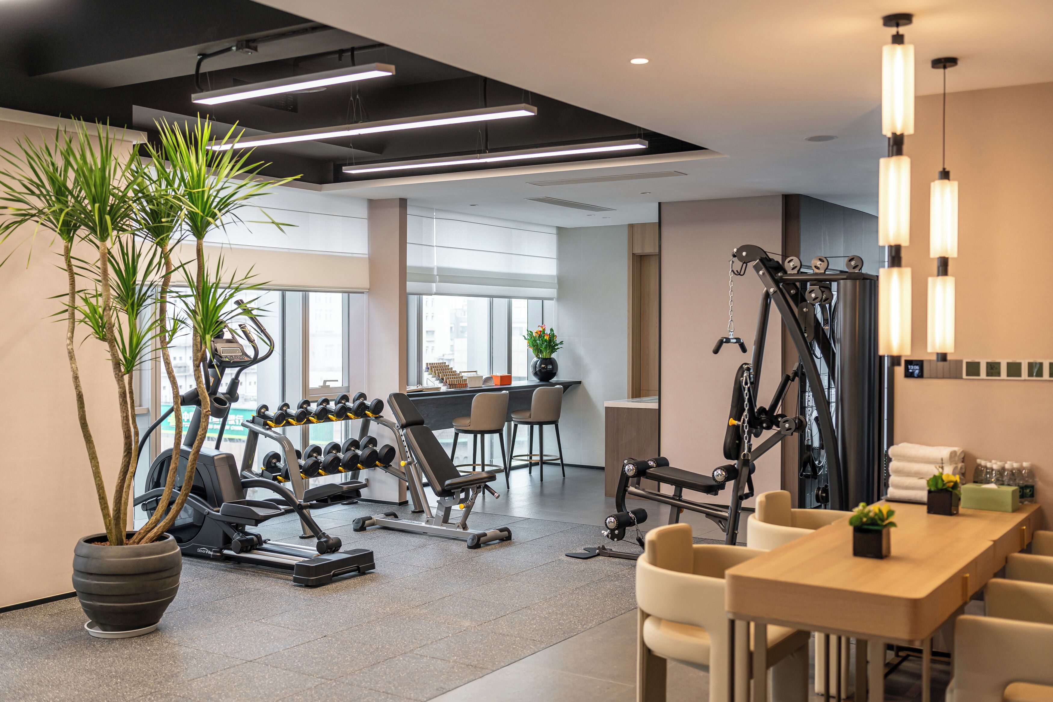 Un gimnasio moderno con equipamiento de ejercicio, un área de comedor y amplias ventanas.