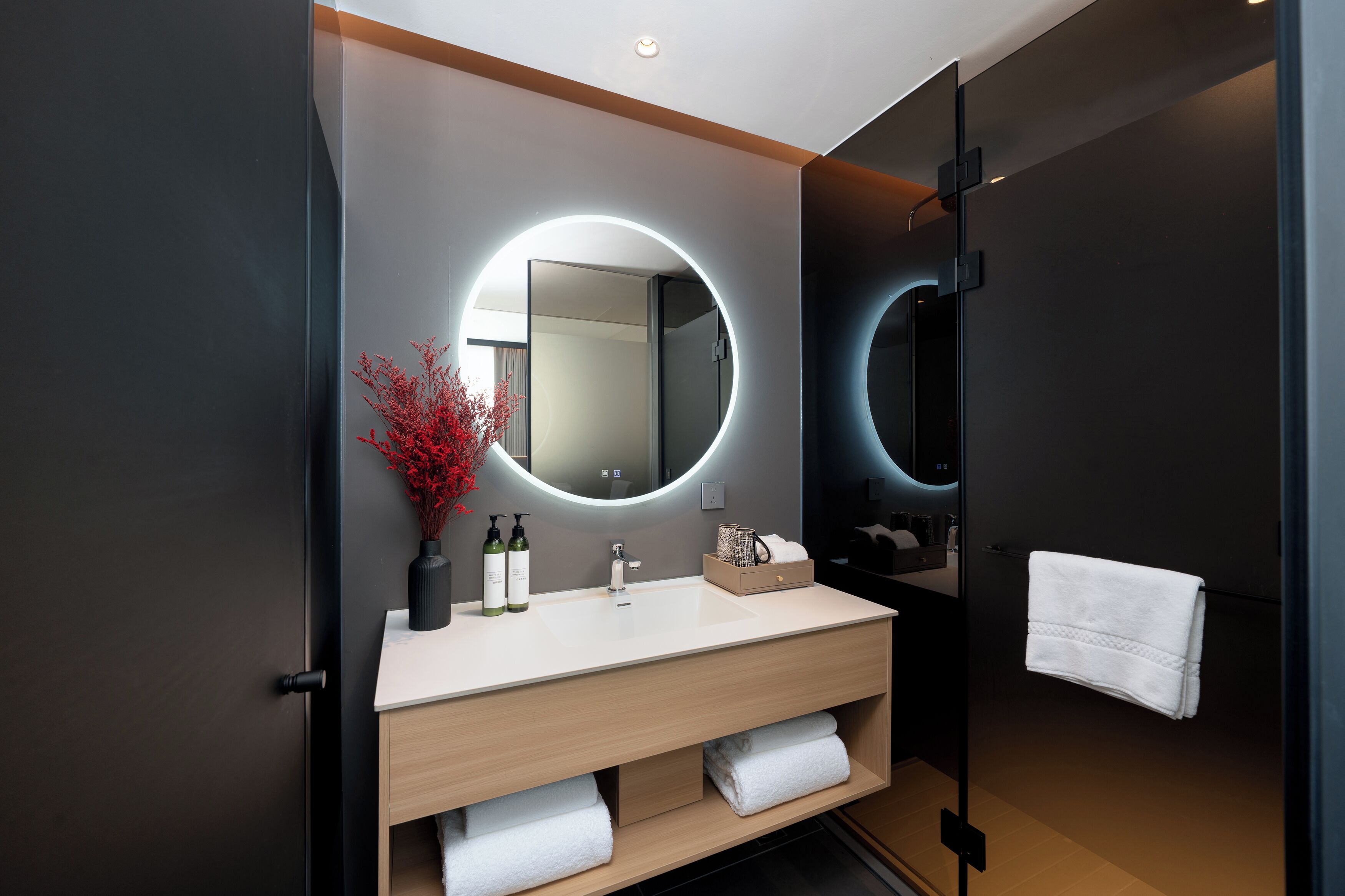 A modern bathroom with a large mirror, a round light, and a towel rack.