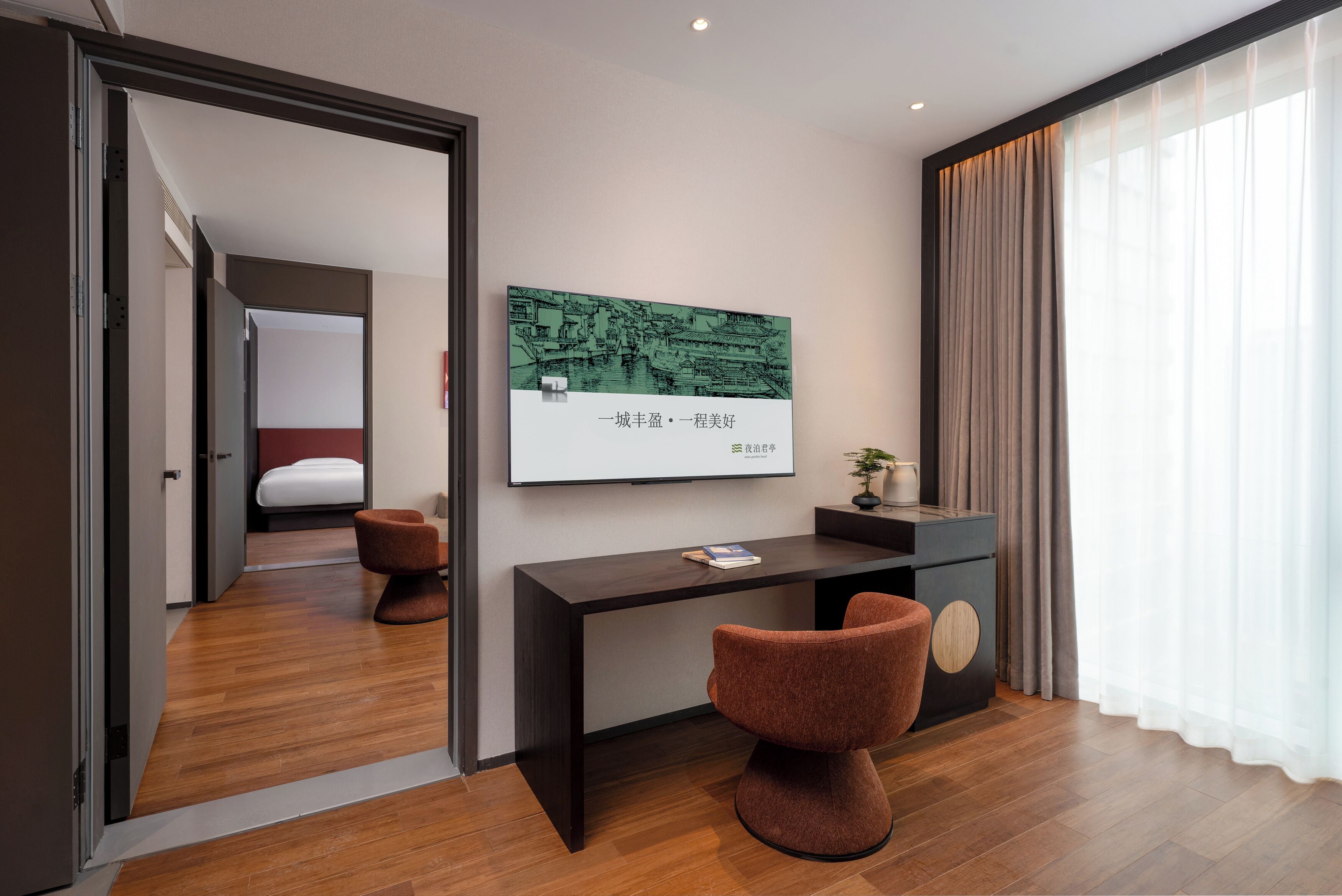 A modern hotel room with a wooden floor, a desk with a chair, a bed, and a large window with curtains.