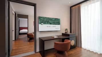 A modern hotel room with a wooden floor, a desk with a chair, a bed, and a large window with curtains.