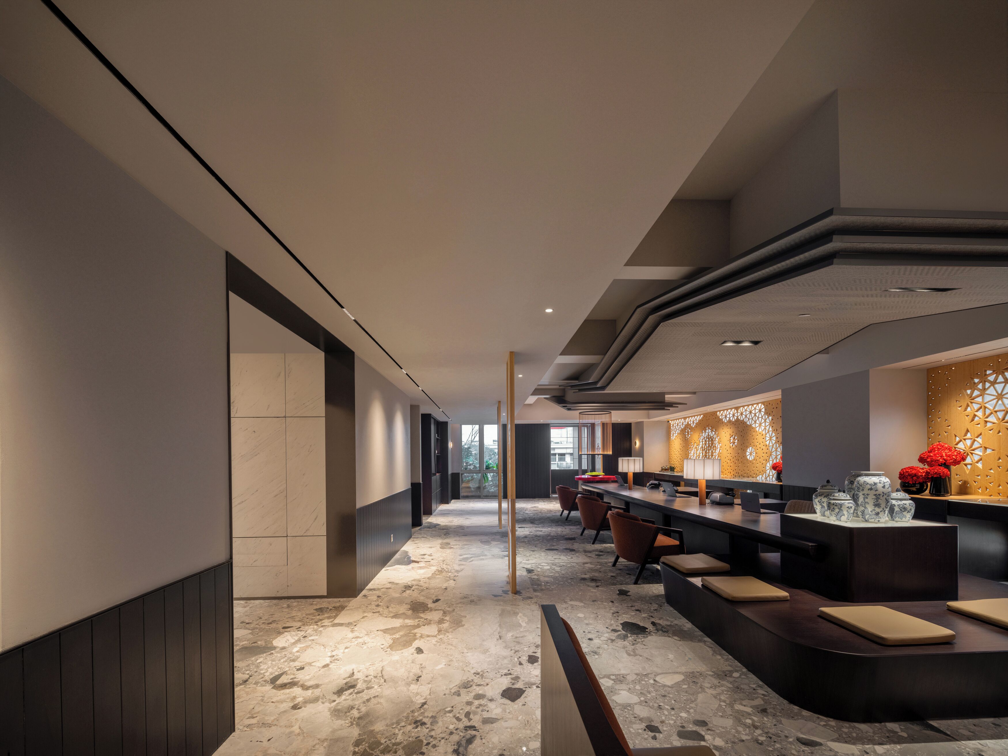 Un moderno vestíbulo de hotel con un mostrador de recepción alargado, zona de estar y una pared decorativa con motivos geométricos.