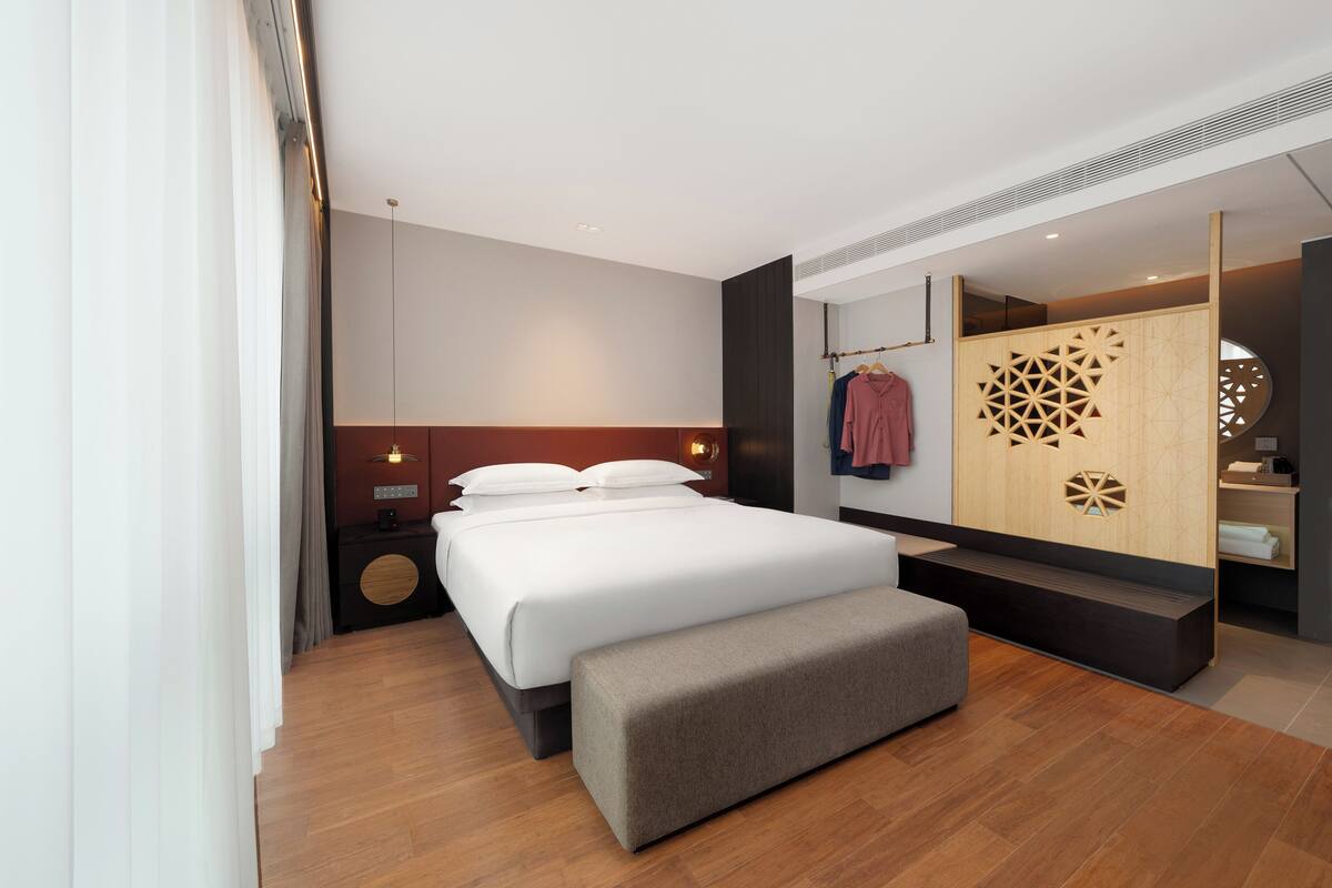 Ein modernes Hotelzimmer mit einem großen Bett, einer Sitzbank, einem Holzschrank und einem Spiegel.