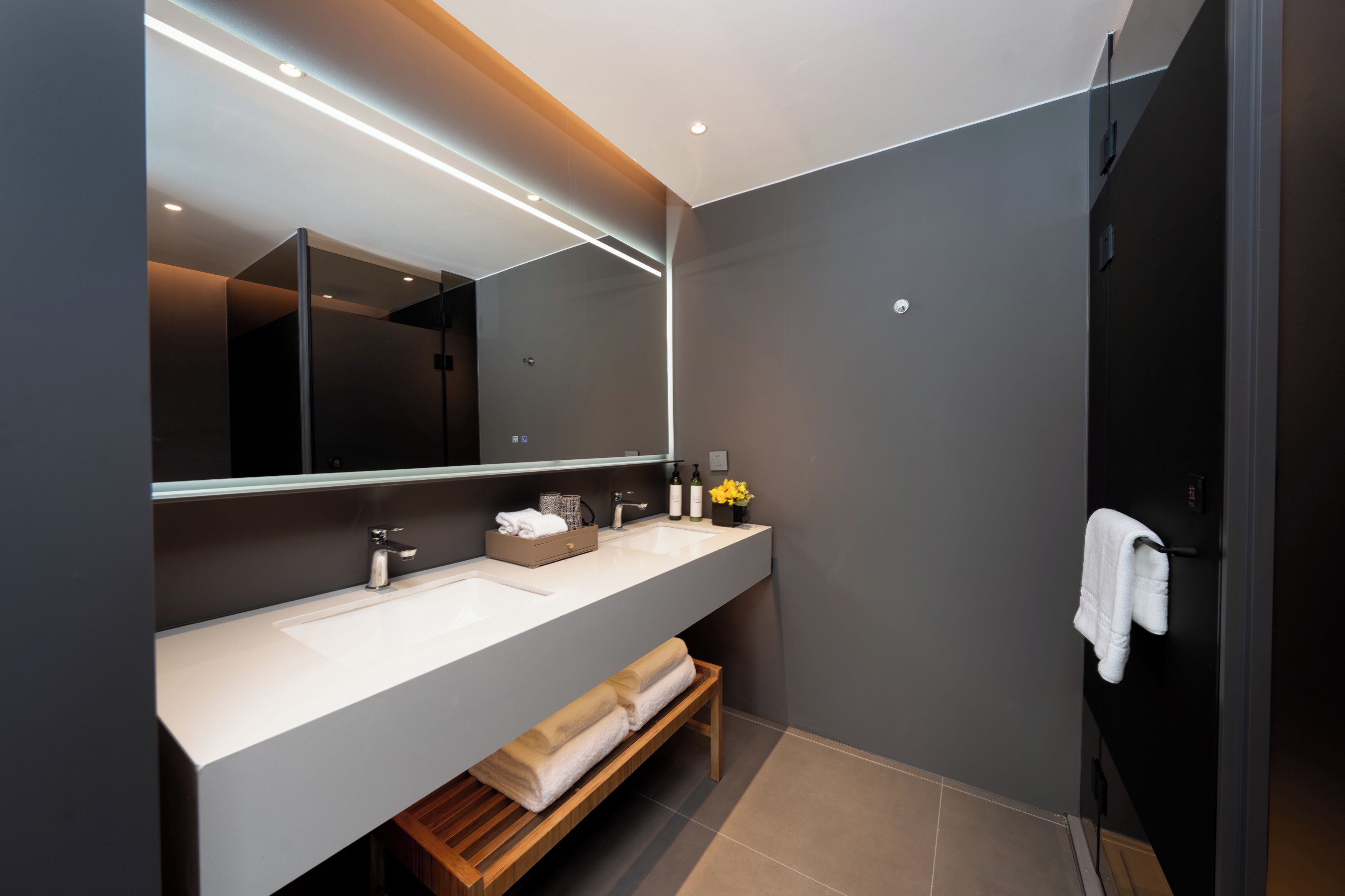 Une salle de bain moderne avec un grand miroir, deux lavabos, un banc et un porte-serviettes.