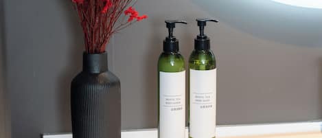 A bathroom vanity with two bottles of white tea body lotion and hand wash, and a vase with red flowers.