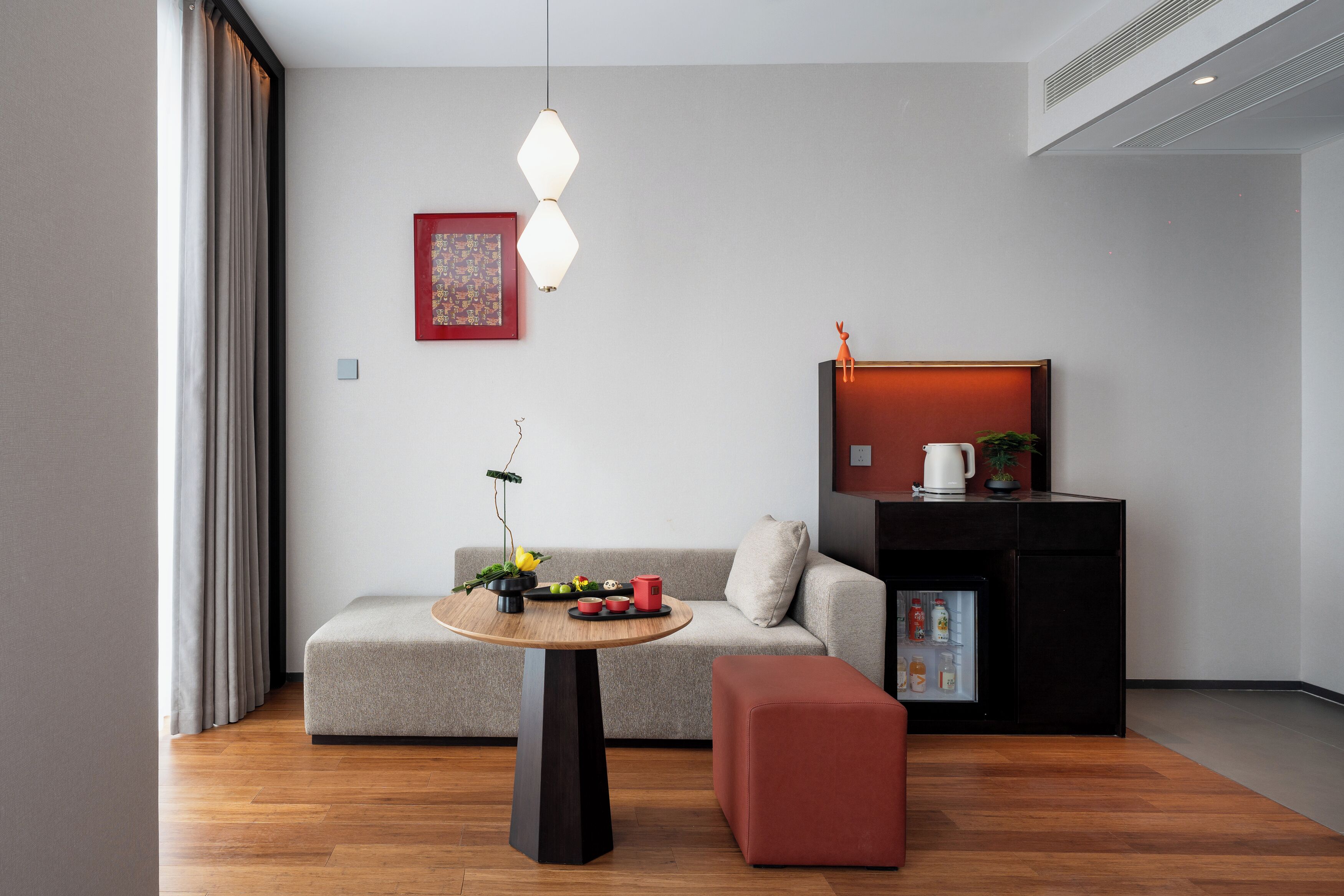 Un salon moderne avec un canapé, une table ronde, un pouf rouge, un meuble noir et une suspension.