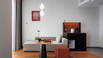 Un salon moderne avec un canapé, une table ronde, un pouf rouge, un meuble noir et une suspension.