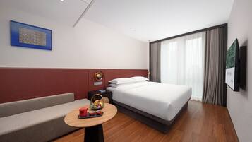 Una habitación de hotel moderna con cama, sofá, una pequeña mesa con frutero y televisor montado en la pared.